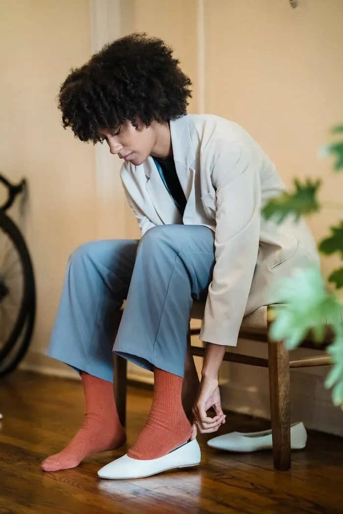 Woman sitting and putting on her white shoes, showing useful facts to prevent blisters.