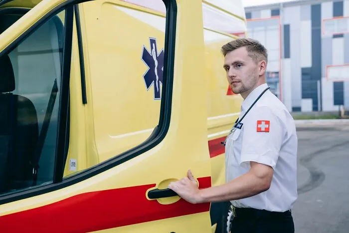 A paramedic opening the door of a yellow ambulance, prepared to act in an emergency.