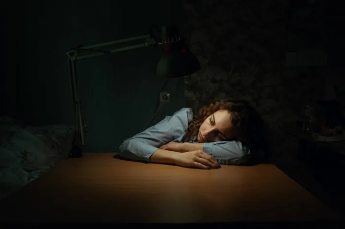 An exhausted woman leaning her head on a table under a desk lamp, reflecting on useful facts.