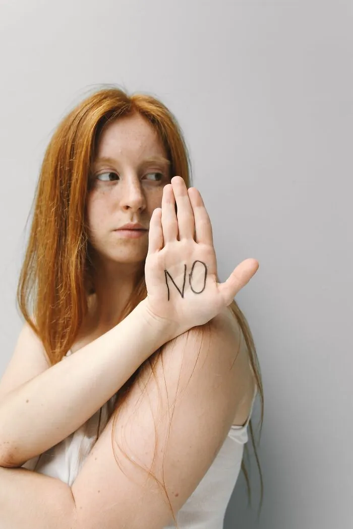 A red-haired woman holding up her hand with NO written on her palm, symbolizing emergency safety and consent.