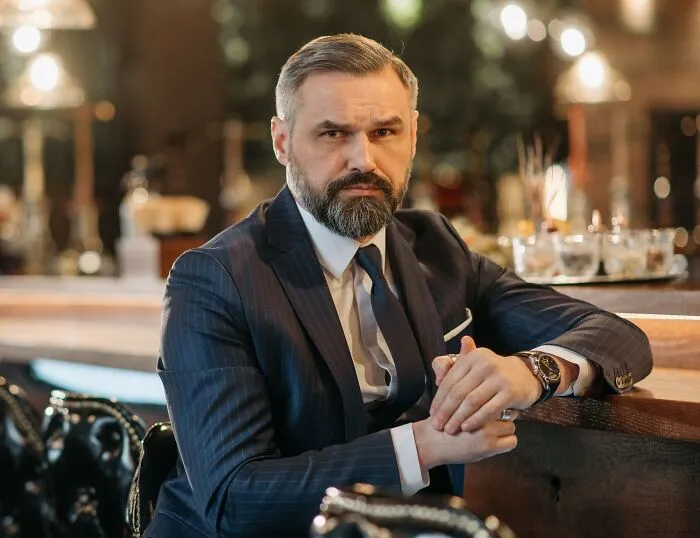 A rich man wearing an elegant dark suit sitting at a bar counter