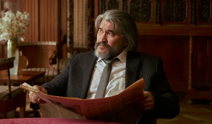 A wealthy senior man with a beard sitting in an armchair and reading a newspaper