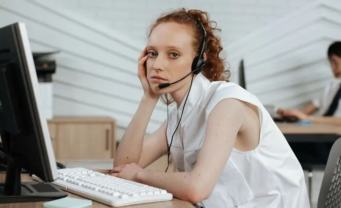 A bored call center worker wearing a headset, listening to complaints and scandals all day long