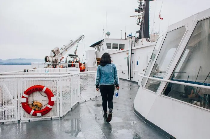 A person in a denim jacket walking on a ferry boat deck during a trip