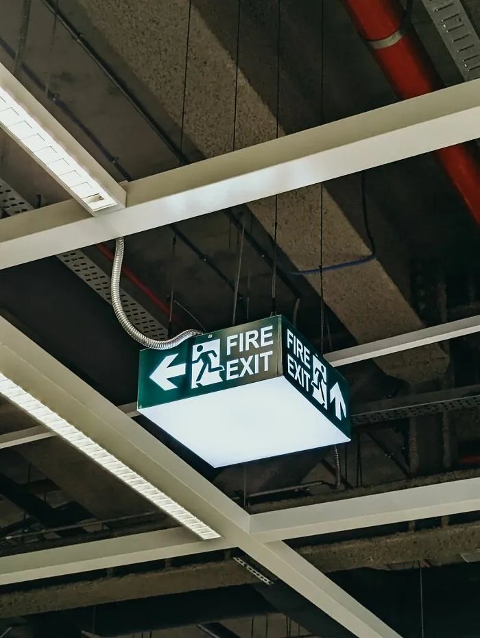 A glowing green fire exit sign hanging from the ceiling during an emergency escape route scenario.