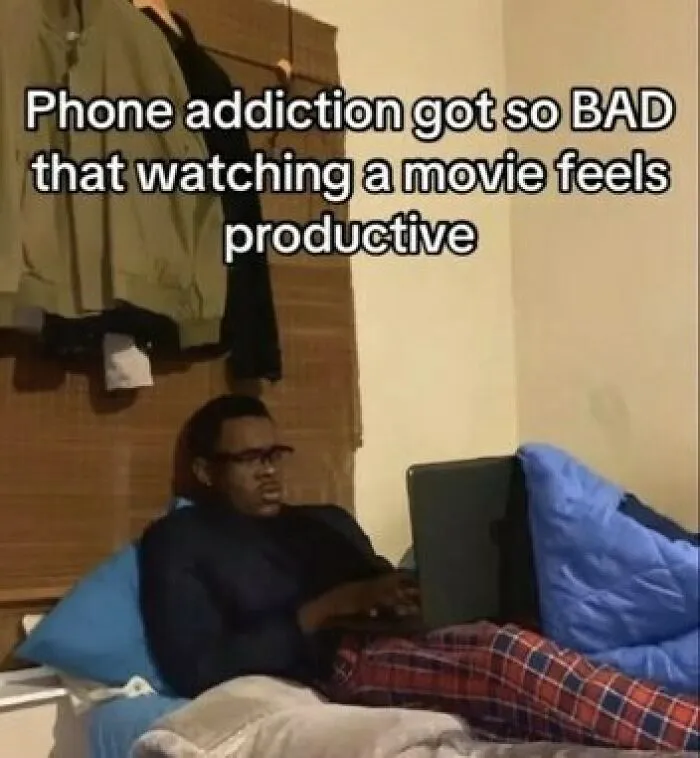 A funny meme about phone addiction showing a man on a bed looking intensely at his laptop screen.