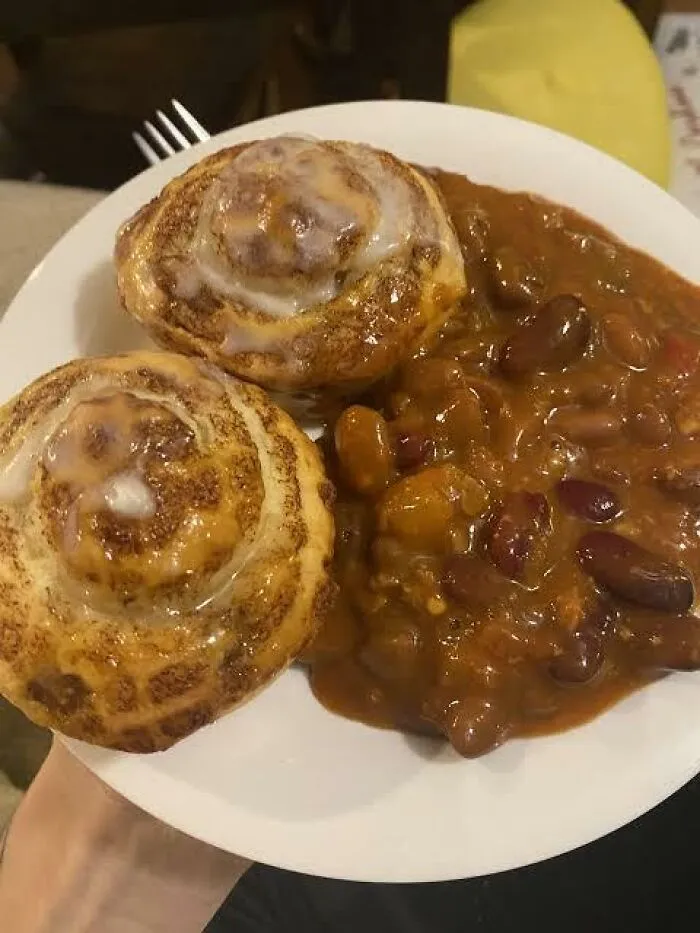 Unusual food combinations of two iced sweet cinnamon rolls served next to a pile of brown chili on a plate