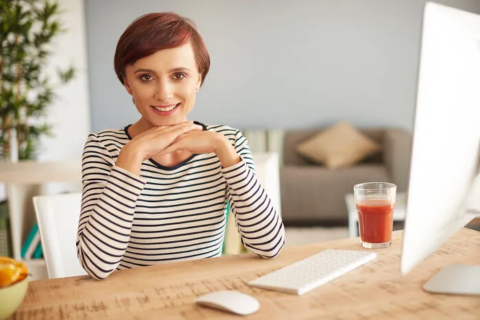 A professional woman smiling at her office desk, discussing how women experience subtle sexism in the workplace.