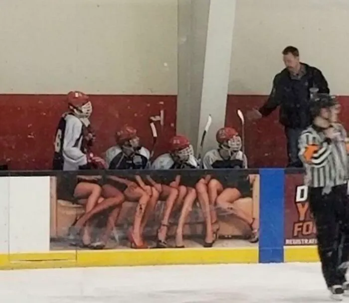 Confusing perspective of hockey players on a bench who appear to have long legs in heels due to a banner advertisement.