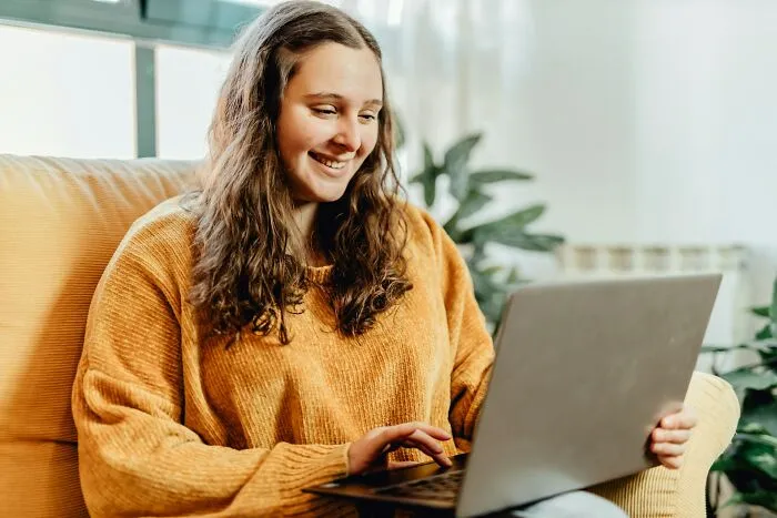 A smiling woman typing on her laptop, searching for creative relationship revenge stories.