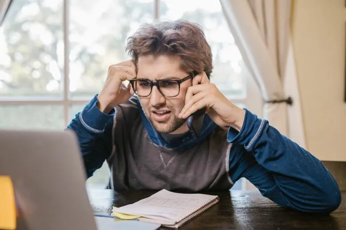 A stressed man on his phone looking at his laptop, perfect for relationship revenge stories inspiration.