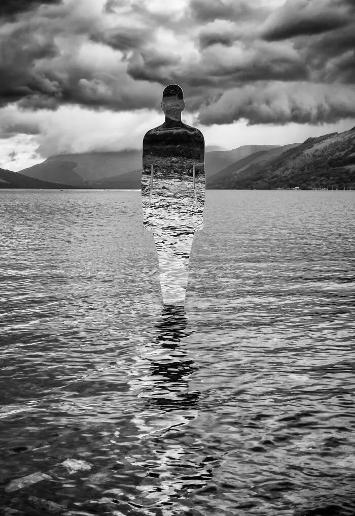 Black and white reflective sculpture standing in rippling lake water under cloudy sky