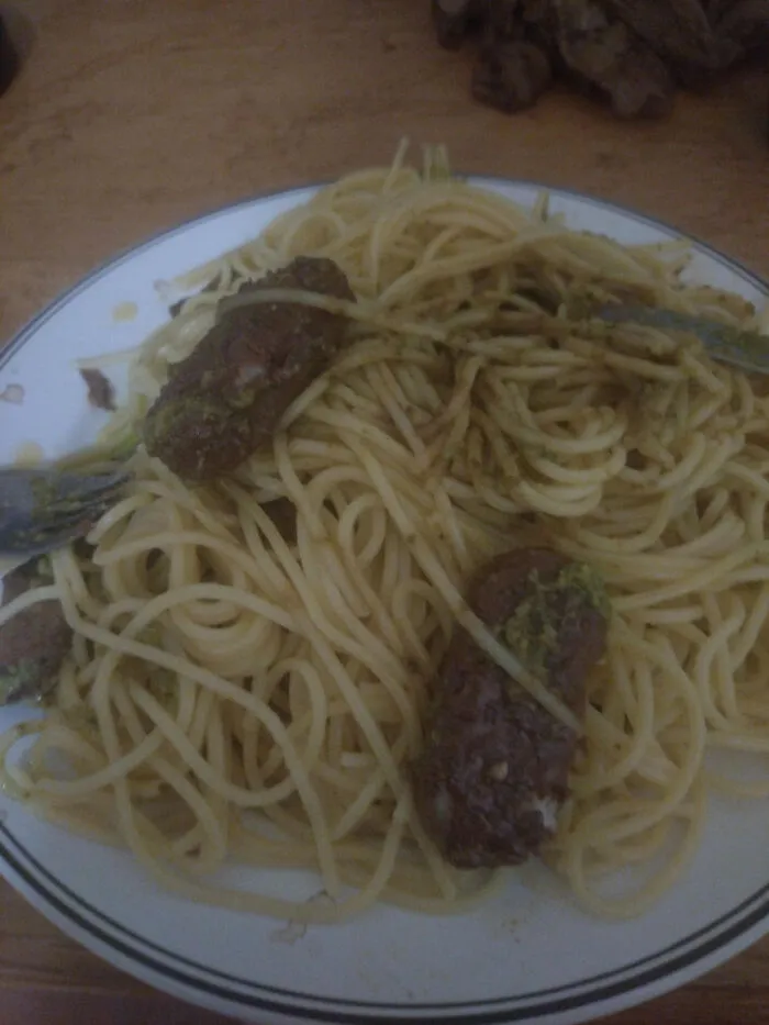 A plate of spaghetti topped with dark, sausage-like pieces showcasing odd food combinations.