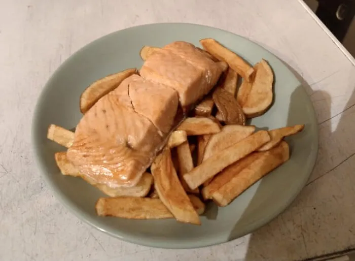 Salmon served over french fries on a plate, a classic example of unexpected food combinations.