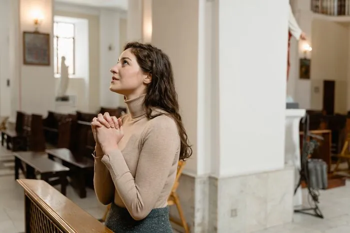 A young woman praying inside a church with folded hands, depicting behaviors of faith and hope