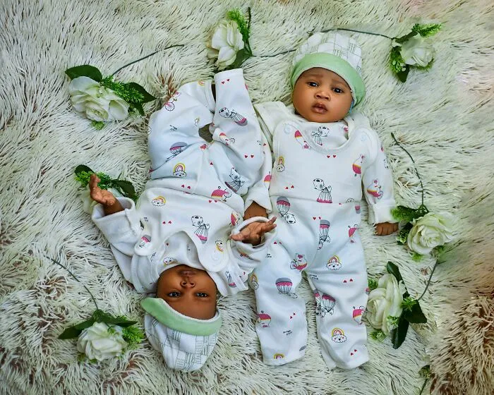 Twin babies dressed in matching outfits lying on cozy blanket surrounded by flowers