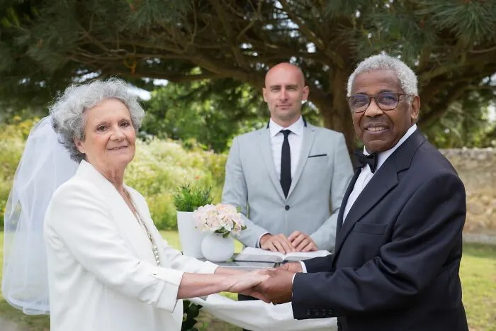 Older couple holding hands at outdoor wedding with man officiating