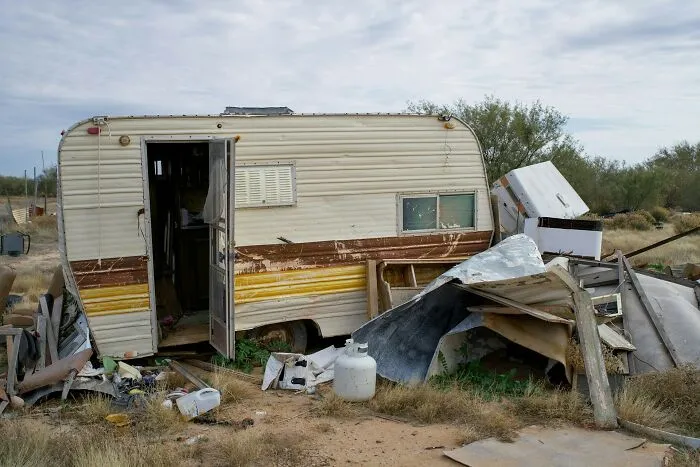 A dilapidated travel trailer with debris around it, symbolizing the weirdest things service workers discover at a client's home.