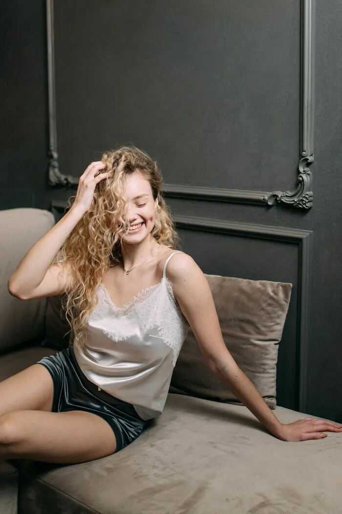 A happy woman with curly blonde hair in pajamas, sitting on a couch, illustrating the weird things service workers walk into.