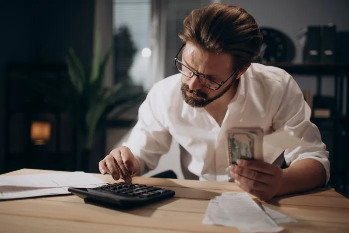 A stressed man calculating his bills and finances, representing the financial strain of divorced people.