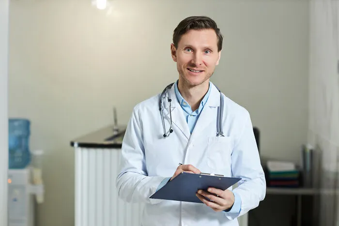 A male doctor in a white coat holding a clipboard, symbolizing healthcare experiences and subtle sexism