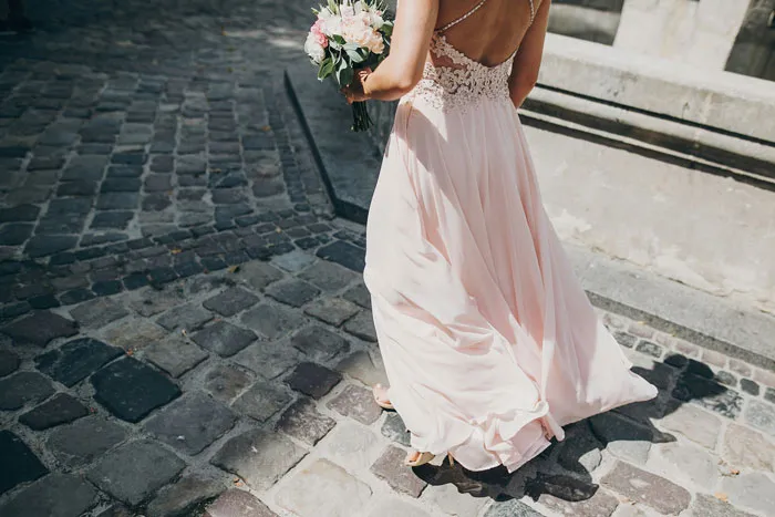 Back view of a bridesmaid in a pink dress holding flowers, walking away during outrageous bridezilla stories.