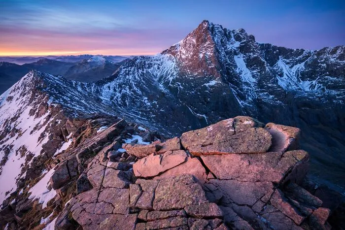 Jagged snow dusted mountain ridge under a colorful dawn sky in natural landscape photography.