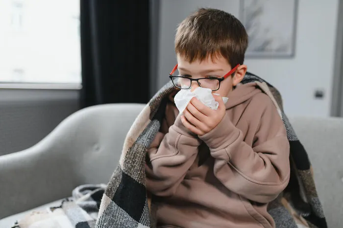 Sick boy blowing nose under blanket at home during the scariest moments of illness