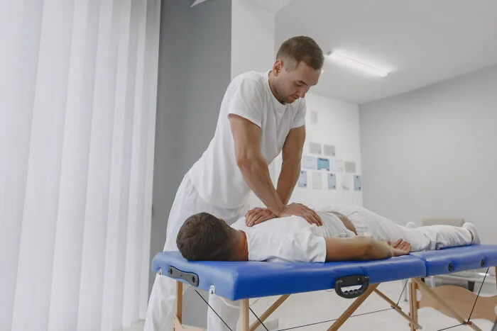 Male physical therapist or doctor treating a male patient on a medical massage table.