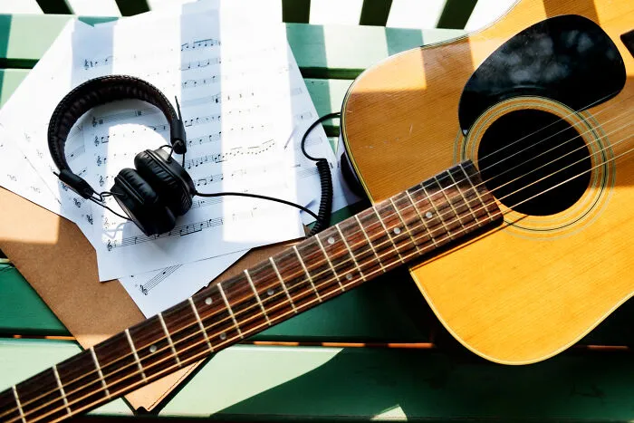 Acoustic guitar alongside headphones and sheet music, symbolizing memorial songs played at funerals