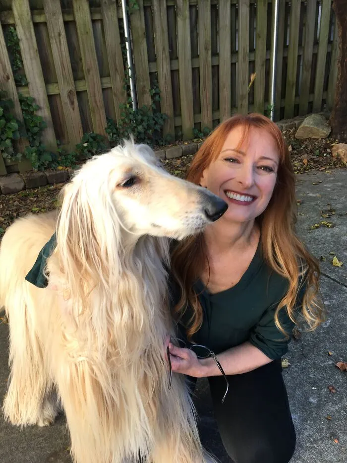 A red-haired woman poses next to her long-haired Afghan hound, showing how pets looked so much like their owners