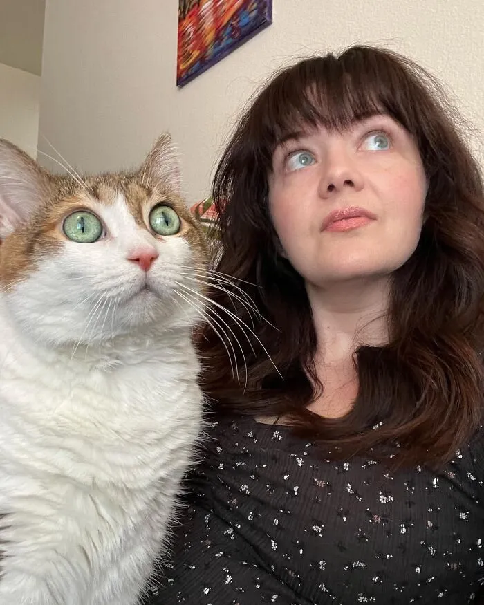 Woman and her pet cat looking upward with matching wide green eyes, showing how pets look like their owners.