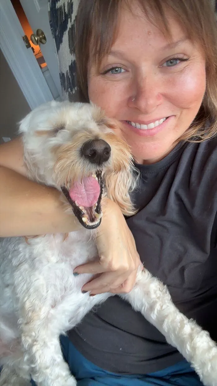 Smiling woman hugging her happy yawning pet dog