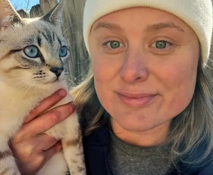 A woman with striking blue eyes posing next to her blue-eyed cat, showing how pets look like their owners.