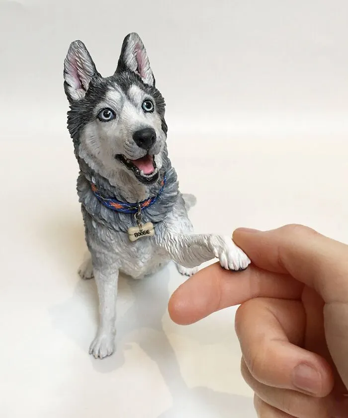 A hand touching the paw of a hyperrealistic sculpture of a husky pet.