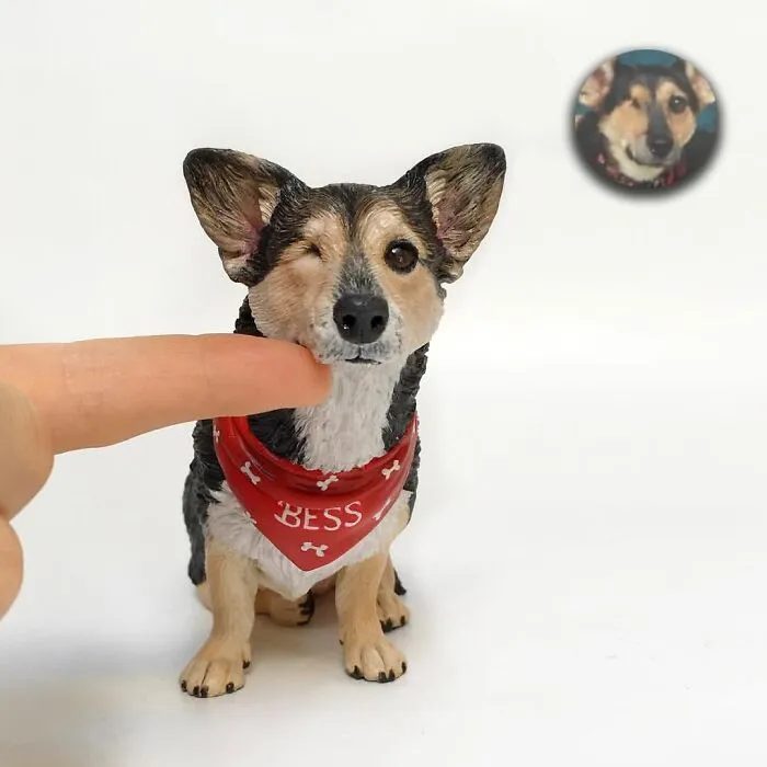 A hand touching a winking dog figure wearing a red bandana, showing hyperrealistic sculptures of pets crafted by an artist.