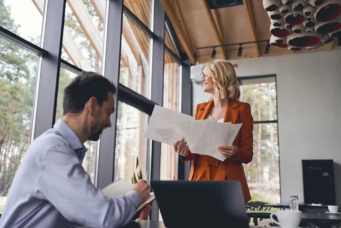 A smiling businesswoman holding papers near a colleague, depicting obvious lies in the workplace