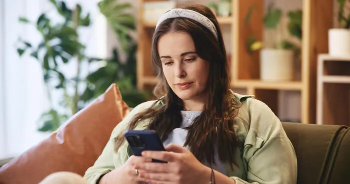 A young woman looks at her phone, feeling sad as her lifelong friendships fizzle out.