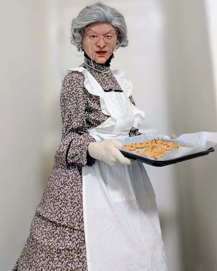 Person dressed in a detailed Mrs Doubtfire grandmother costume holding a tray of cookies for creative Halloween costume ideas.