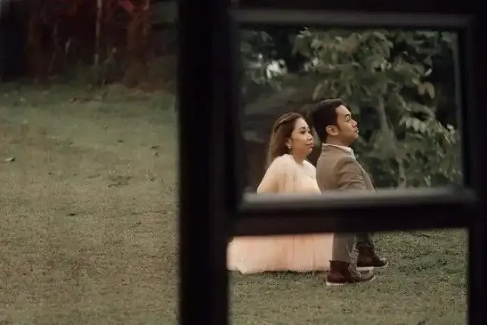 A couple posing outdoors seen through a window frame in a perfectly confusing optical illusion.