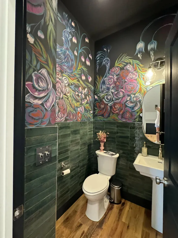 A powder room homes makeover featuring dark green tiles and hand-painted wall art.