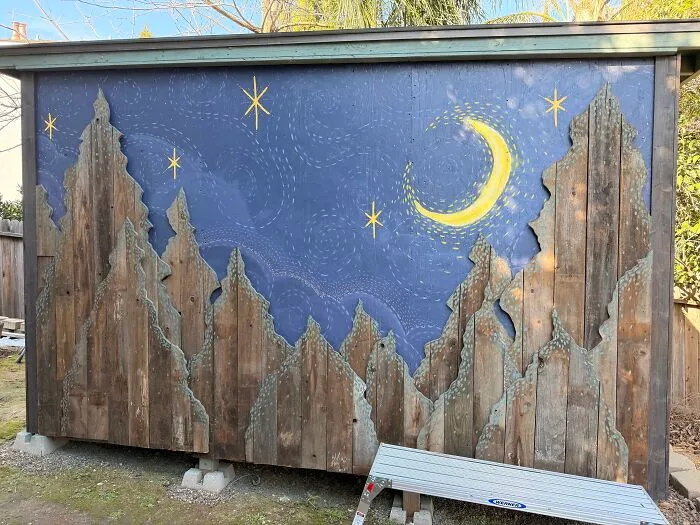 Outbuilding wall decorated with wooden pine tree cutouts and night sky painting, using creativity to save money.