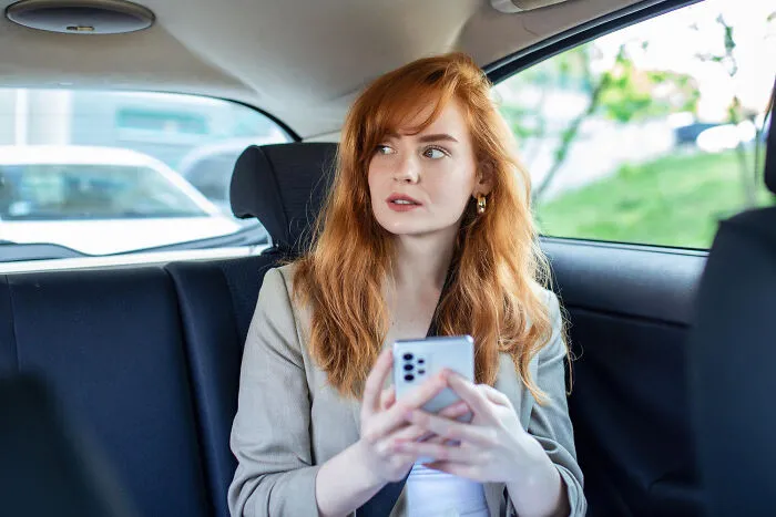 A red-haired woman sitting in a car using her smartphone, wondering why people decide to skip a second date.