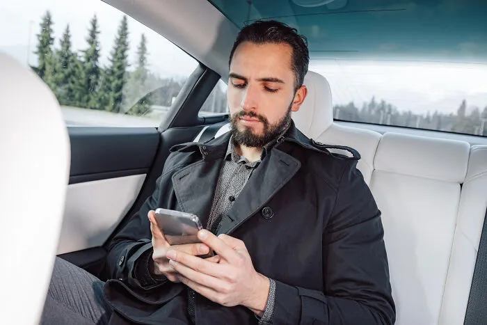 A man looking at his phone in a luxury car, reflecting on whether to skip a second date.