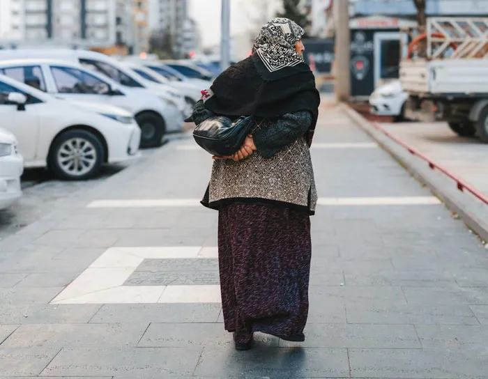 Elderly woman walking past parked cars, feeling her fight-or-flight activate around strangers