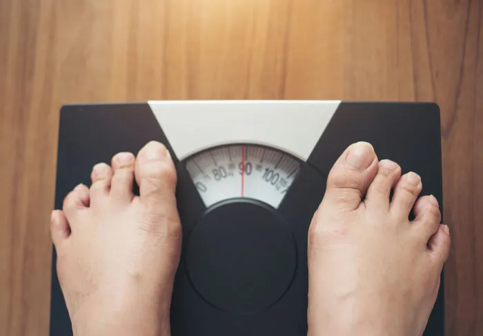Top-down view of feet standing on a weight scale, symbolizing hilariously obvious lies about weight loss
