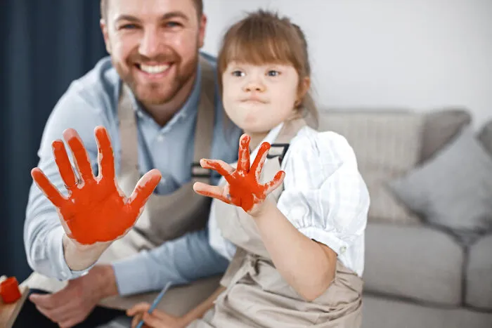 A smiling father and daughter with down syndrome showing orange painted hands during a fun art activity
