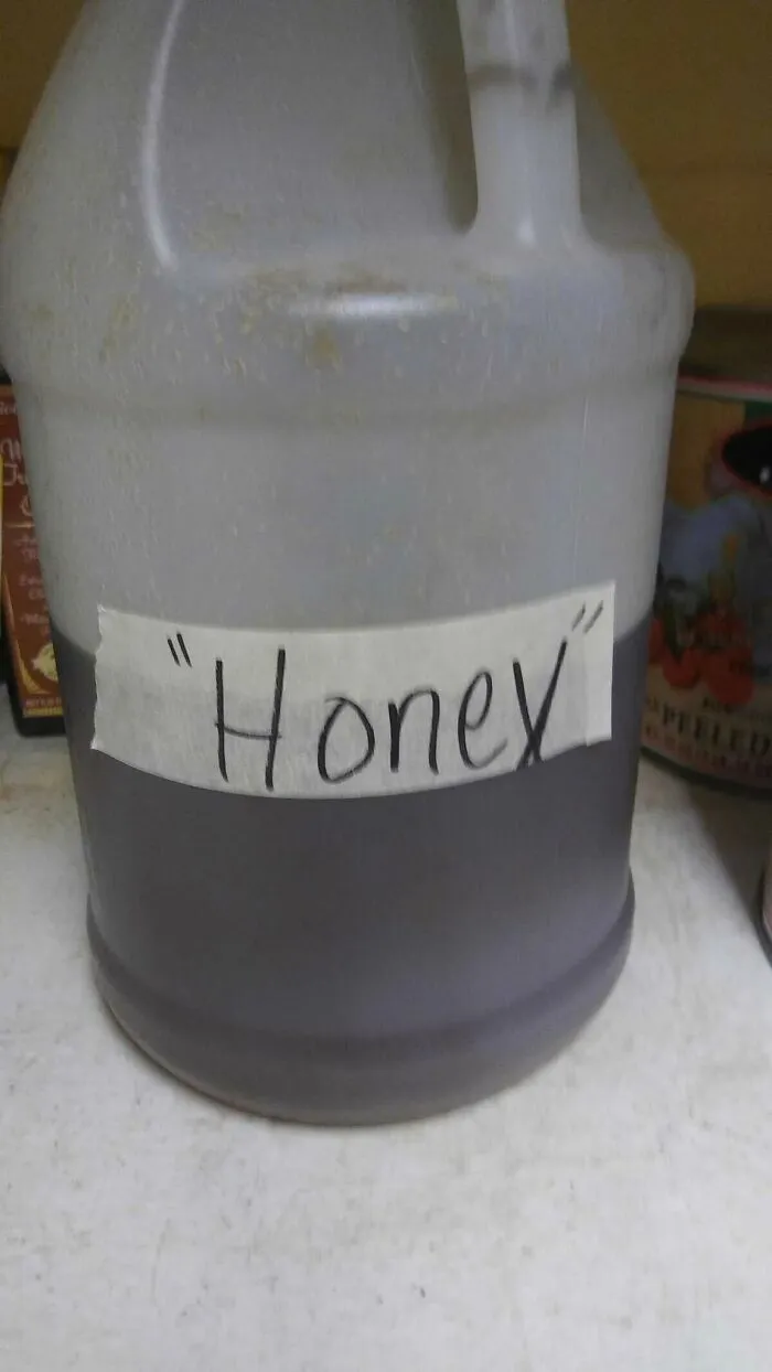 A plastic jug with a tape label misusing quotation marks around the word honey.