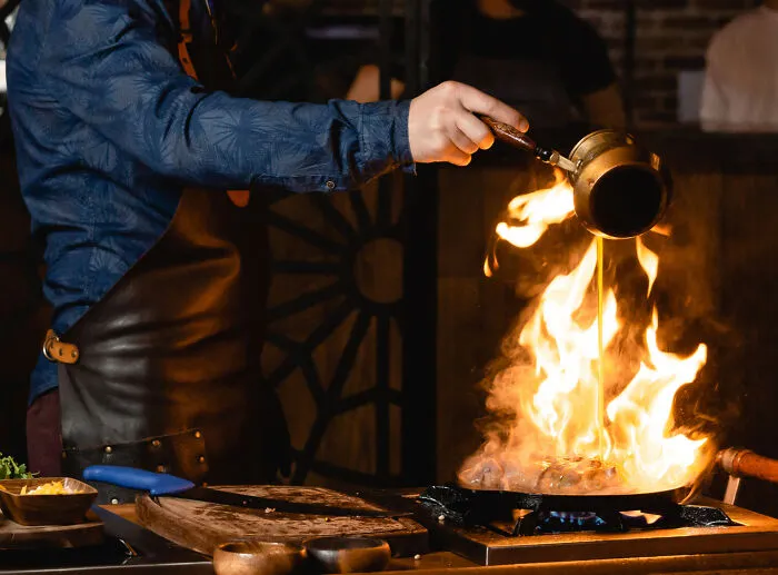 A chef pouring liquid into a flaming pan, illustrating kitchen safety and cooking emergency tips.