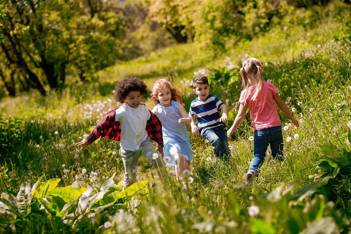 Group of young children playing and running in a grassy field, showcasing the start of lifelong friendships.